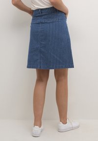 Mörkblå denimkjol med vita vertikala ränder, utrustad med en åtsittande midja och bakfickor, i kombination med vita sneakers.