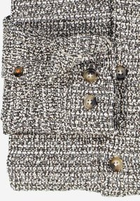 Strickjackenstoff in Schwarz und Weiß, mit großen braunen Knöpfen und strukturiertem Oberflächenmaterial. Enthält Taschen mit Knopfverschlüssen.