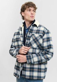 Veste en flanelle à carreaux dans des tons de bleu, blanc et marron, dotée d'un col en polaire doux et d'une poche poitrine boutonnée. Tissu texturé.