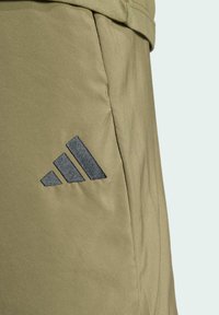Pantalones cortos deportivos color caqui con una tela suave, bolsillos laterales y un logo de adidas en gris oscuro en la pierna izquierda, con un diseño minimalista.