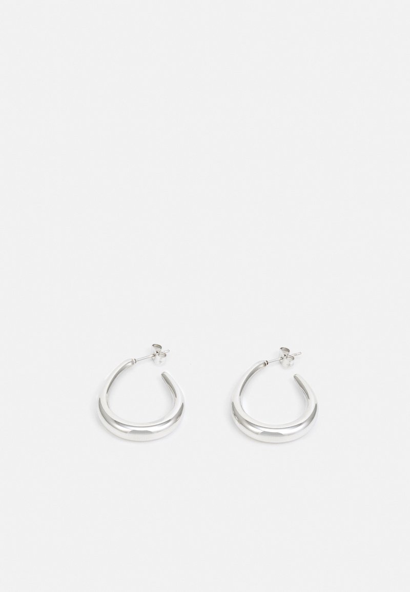 Paire de petites boucles d’oreilles anneaux épaisses en argent avec extrémités ouvertes et fermoir papillon sur fond blanc.