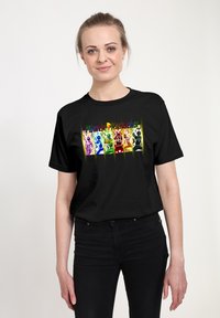 Kvinde iført en sort T-shirt med seks farverige Power Rangers i aktion under "Power Rangers"-logoet.