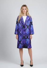 Abrigo de patrón morado y negro con corte largo, solapas grandes y dos botones. La tela tiene una textura suave, con intrincados remolinos.