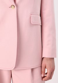 Blazer rosa chiaro con tessuto testurizzato, chiusura con un solo bottone e tasca strutturata con dettaglio di cucitura a contrasto.