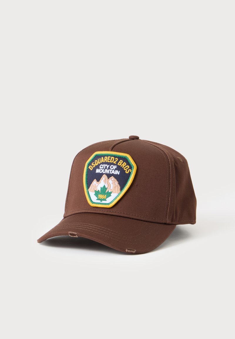 Casquette de baseball marron avec un écusson montrant des montagnes, une feuille d'érable verte et le texte "DSQUARED2 BROS CITY OF MOUNTAIN 1964" sur le devant.