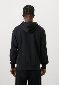 Czarny sweter z kapturem i sznurkiem, z ribbowanym wykończeniem rękawów i dolnej części, wykonany z miękkiego materiału. Charakteryzuje się luźnym krojem i minimalistycznym designem.