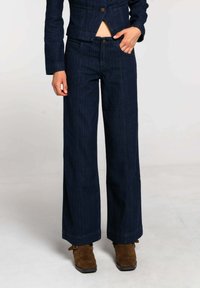 Pantalones anchos de mezclilla azul oscuro con cintura alta, costuras visibles, dos bolsillos frontales y cierre de botón. Tela texturizada y corte entallado.