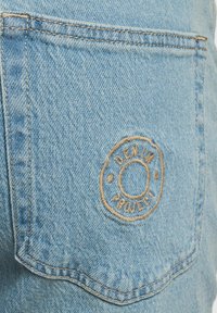 Lys blå denim stoff med en lomme med brodert logo "DENIM PROJECT" i beige tråd. Klassisk jeans tekstur.