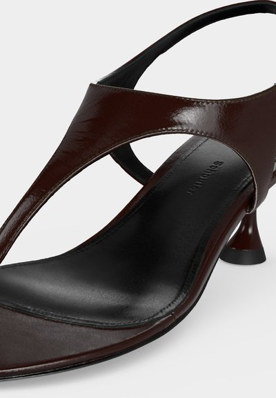 Ciemnobrązowa skórzana sandałka z odkrytymi palcami, paskiem z tyłu i niskim obcasem w kształcie klepsydry na czarnej podeszwie, ukośne zbliżenie.