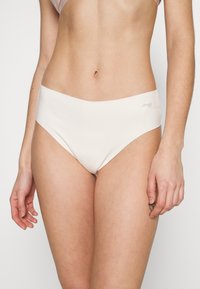 Culotte seamless taille haute en beige clair ; texture lisse avec un design minimaliste. Branding subtil visible sur la ceinture.