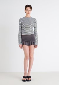 Pruhovaný top s dlouhým rukávem v černé a bílé barvě doplněný šedou mini sukní s volánkovým lemem; model má na sobě černé platformové boty.