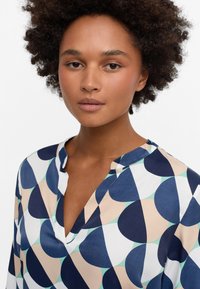 Gemusterte Bluse in einem Mix aus Marineblau, Pfirsich und Weiß mit geometrischen Formen. Hergestellt aus glattem Stoff, mit einem Kragen im Notch-Stil und lässiger Passform.