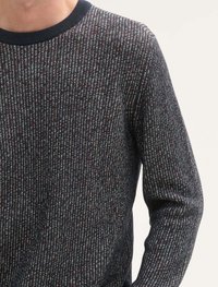 Pull en maille de couleur bleu nuit avec des éclats rouges, verts et blancs. Présente une texture côtelée et un col rond avec une encolure solide de couleur foncée.
