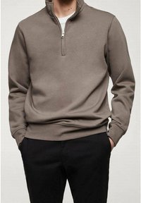 Pull à col zippé gris en tissu doux, avec une texture brossée, des manches longues, des poignets côtelés et une coupe décontractée, associé à un pantalon sombre.