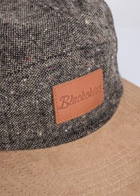 Brown bucket hat featuring a textured fabric upper with multicolored flecks and a tan leather patch logo on the front.