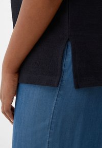 Črn teksturiran top z bočnimi razpoki, v kombinaciji z modrim jeans krilom. Top ima rebrast zaključek in sproščen kroj.