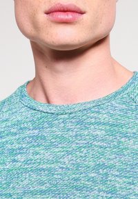 Zeleno-modré směsové bavlněné pletené tričko s kulatým výstřihem a texturovaným povrchem, vybavené krátkými rukávy a volným střihem.