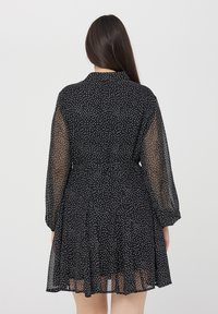 Abito nero con pois bianchi, realizzato in tessuto leggero e trasparente. Presenta maniche lunghe, vita cin cin e gonna svasata.