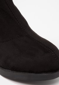Stivale alla caviglia in suede nero con punta rotonda, texture liscia e dettagli di cucitura visibili. La suola è piatta e realizzata in gomma.