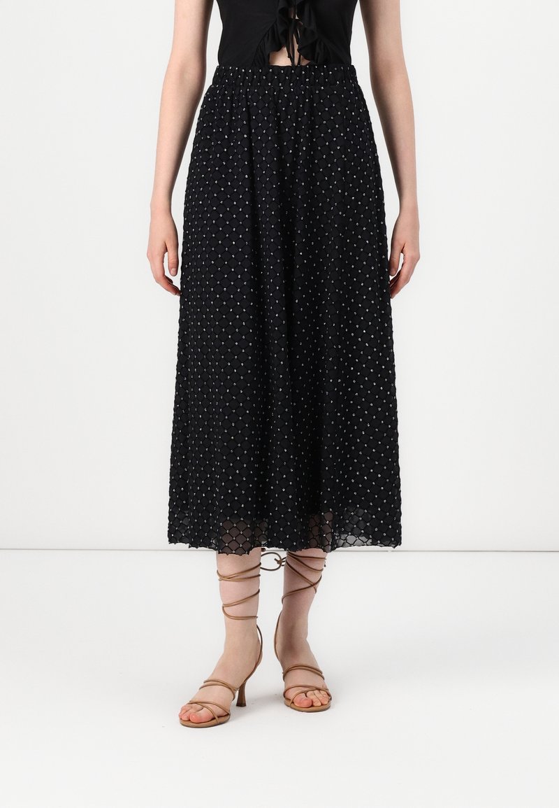 Jupe midi noire à motif pois texturé, associée à des sandales à talons hauts nude à brides et un crop top noir noué.