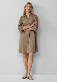 Abito marrone fino al ginocchio con colletto e maniche a tre quarti; tessuto fluido, tasche laterali e design minimalista.
