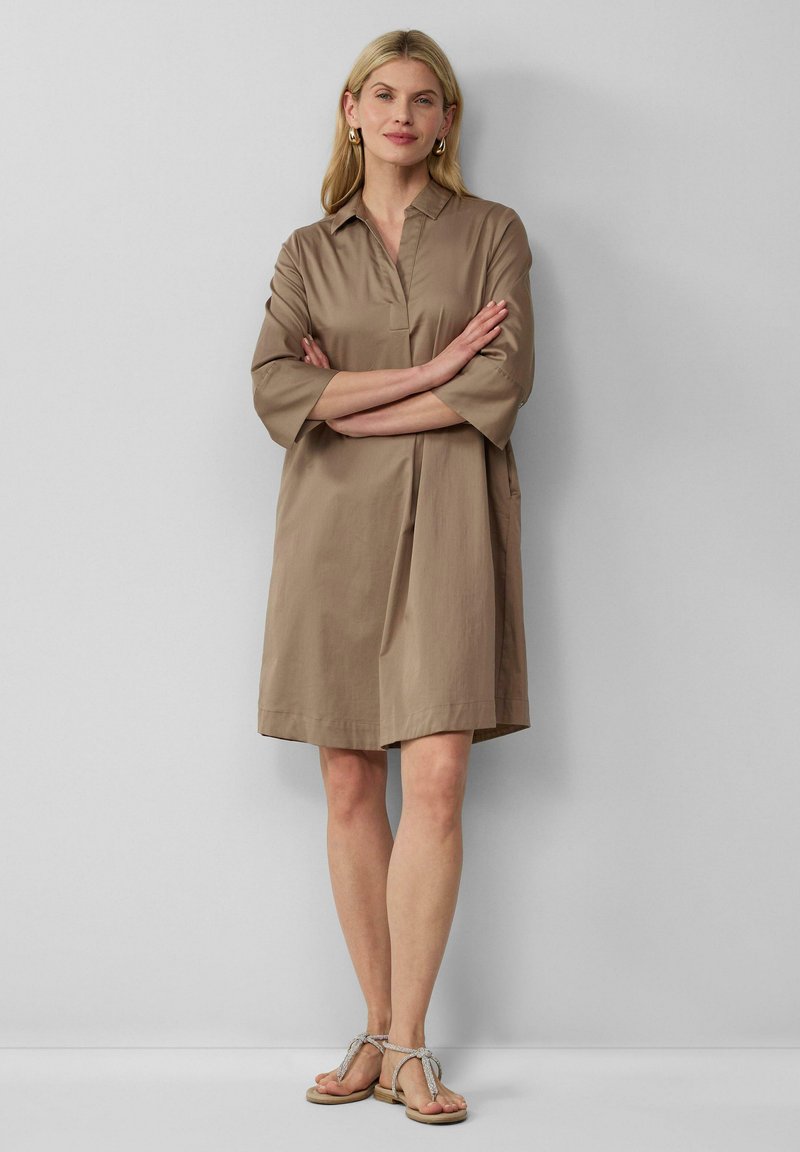 Abito marrone fino al ginocchio con colletto e maniche a tre quarti; tessuto fluido, tasche laterali e design minimalista.