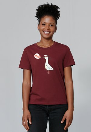 T-shirt en coton bordeaux avec un dessin de mouette en bande dessinée portant un chapeau et une bulle de dialogue disant "MAMAN". Design à manches courtes et col rond.