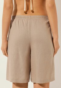 Pantalones cortos de lino beige con cintura elástica, corte recto y aberturas laterales en el dobladillo para mayor libertad de movimiento.