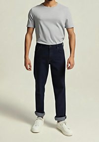 Camiseta gris de manga corta combinada con vaqueros azul oscuro con puños ligeramente doblados y zapatillas blancas, que muestra un diseño de conjunto casual.