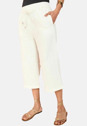 Pantalon blanc court à jambes larges avec taille élastique et cordon, porté avec des sandales plates dorées à brides et un haut noir.