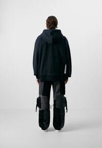 Fekete, oversized kapucnis pulóver, laza fekete és szürke cargo nadrággal párosítva, amely zsebekkel és húzózsinórokkal rendelkezik. Sima textúra, laza design.