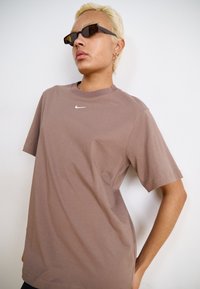 Rjava kratkosleečna majica Nike s krojenjem okroglega izreza, na sredini prsnega dela pa je majhen bel logotip. Gladka bombažna tekstura.