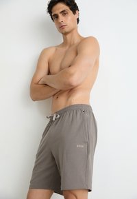 Grå shorts laget av myk stoff med elastisk midjebånd og snor, med en subtil logo på venstre side.