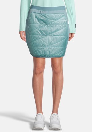 A teal insulated skirt with a quilted pattern and a wide elastic waistband, paired with white athletic shoes.