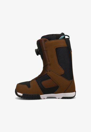 Brauner und schwarzer Snowboardstiefel mit einer weißen Sohle, Drehverschluss-System und blauer Zuglasche hinten, seitlich auf weißem Hintergrund dargestellt.