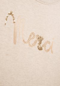 Beige Baumwoll-Sweatshirt mit dem Wort "Merci" in goldfarbenem Metallfaden und glänzenden goldenen Pailletten, die einen Teil des Textes veredeln.