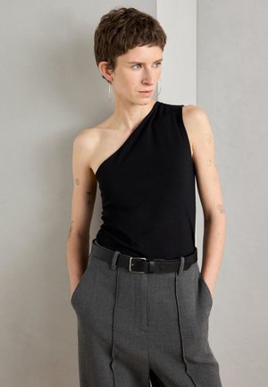 Black, one-shoulder top made of smooth fabric, paired with high-waisted, light gray trousers featuring pleats and a black belt.