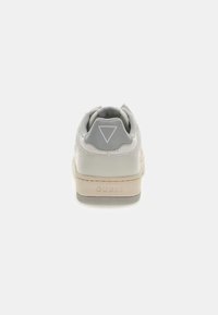 Białe sneakersy z szarym teksturowanym overlayem, kremową podeszwą, zaokrąglonym kształtem i wytłoczoną na pięcie nazwą „GUESS”. Logo w kształcie trójkąta z tyłu.