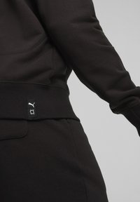 Felpa nera con orlo e polsini a coste, dotata di un piccolo etichetta nera con il logo Puma. Tessuto morbido, design aderente.