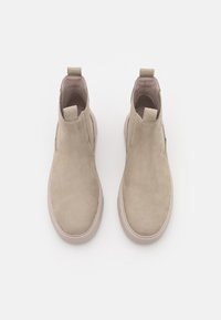 Beige Wildleder-Stiefeletten mit glatter Oberfläche, elastischen Seitenpaneelen und Ziehschlaufen; abgerundete Zehenpartie und eine flache, beige Gummisohle.