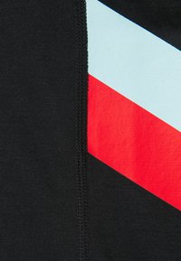 Zbliżenie czarnej tkaniny z pionowym szwem i ukośnymi niebieskimi oraz czerwonymi paskami po prawej stronie.