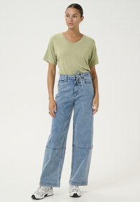 Tricou verde deschis cu guler în V și mâneci scurte, asortat cu blugi din denim albastru deschis, cu talie înaltă și pantalonii largi, având un cordon la talie.