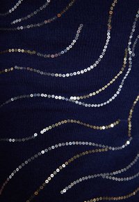 Tessuto blu navy con motivi ondulati di paillettes argento, oro e rosa, che creano una superficie testurizzata e scintillante.