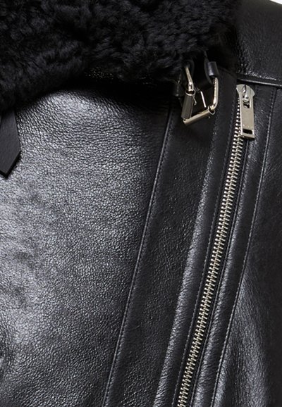 Sort læderjakke med en tekstureret faux fur-krave, sølvlynlåse og kontrastmatte accenter. Nærbillede af de detaljerede materialer.