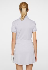 Ljuslila golfklänning med polo-krage, korta ärmar och elastisk midja. Texturen ser slät ut. Baksidan visar logodetalj.