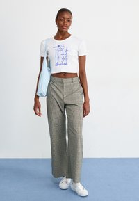 Hvid cropped t-shirt med blå grafisk print, ternede bredbenede bukser i grøn, beige og orange samt hvide sneakers. Lys blå skuldertaske.