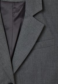 Grauer Blazer mit Reverskragen, subtiler Struktur und einer einzelnen Brusttasche, mit einem dunkleren, glatten Innenfutter.