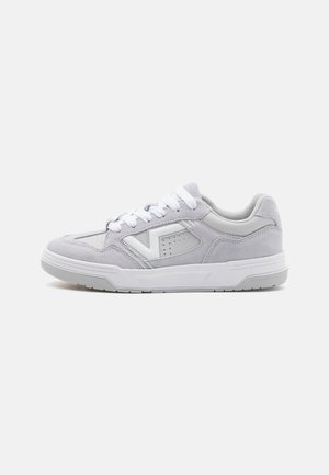 Sneaker grigio chiaro realizzato in suede e pelle, con una suola in gomma bianca, lacci bianchi e un design decorativo con perforazioni sui lati.
