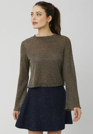 Haut métallisé bronze à manches longues avec un col rond et un ourlet effiloché, associé à une jupe texturée bleu marine avec des paillettes dorées.