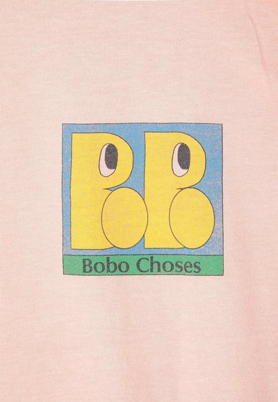 Lettres B stylisées jaunes avec des yeux sur un fond carré bleu au-dessus d'un rectangle vert avec le texte Bobo Choses sur un tissu rose clair.